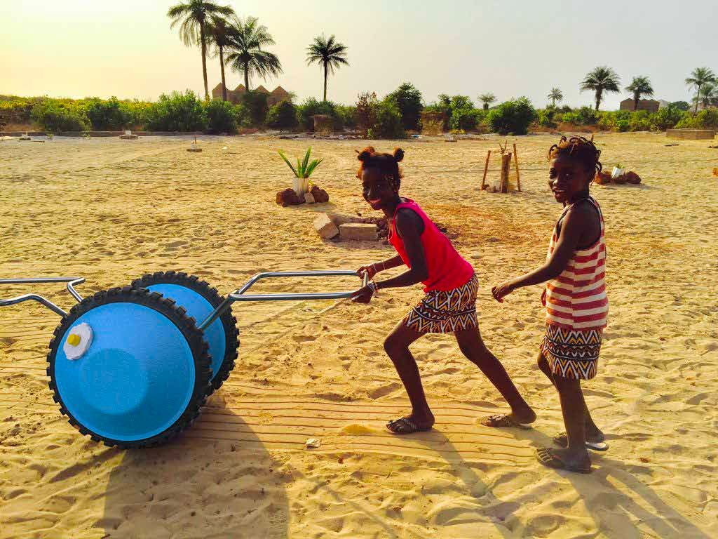 Two children pulling a water roller across sand